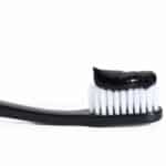 black plastic toothbrush with black charcoal paste on white background