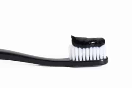 black plastic toothbrush with black charcoal paste on white background