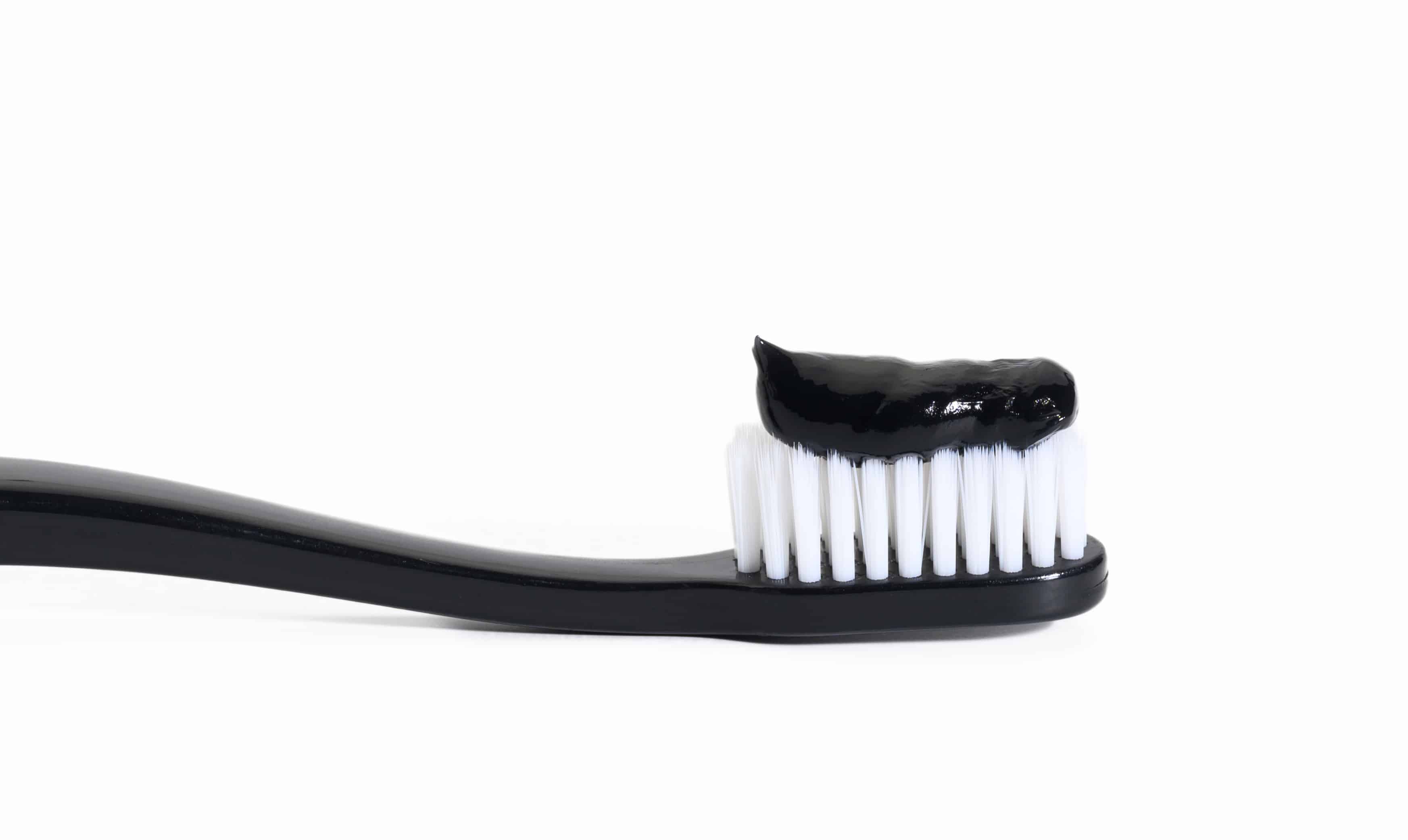 black plastic toothbrush with black charcoal paste on white background
